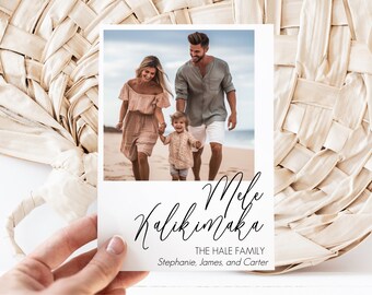 May include: A white card with a family photo on the beach. The card has the words "Mele Kalikimaka" in script, along with "THE HALE FAMILY" and names. The card is held in front of a woven background.