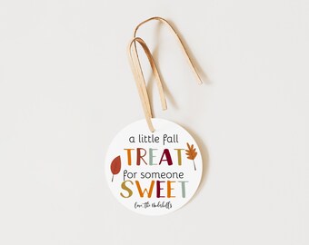 May include: A round white gift tag with a tan leather cord. The text reads a little fall TREAT for someone SWEET, followed by Love, the Underhills. The design features small autumn leaf illustrations in red, orange, and brown colors.