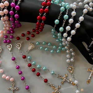 May include: A set of five pearl rosaries with silver crosses and charms. The rosaries are in pink, purple, red, blue, and white.