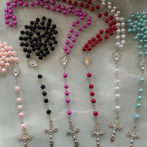 May include: Six different coloured rosary necklaces with silver crosses. The rosaries are pink, black, purple, red, white and blue.