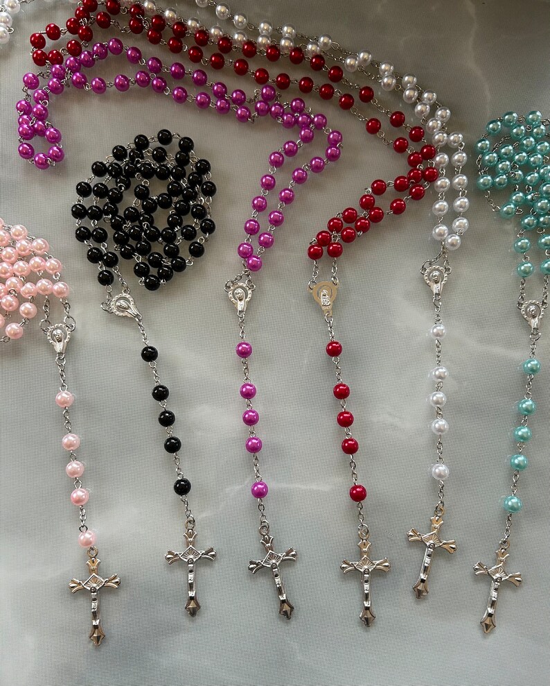 May include: Six different coloured rosary necklaces with silver crosses. The rosaries are pink, black, purple, red, white and blue.