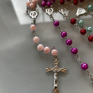 May include: A silver rosary with a crucifix and beads in pink, purple, red, and blue.