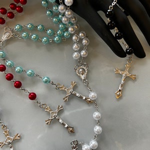 May include: Five different rosaries with silver crosses and beads in red, white, black, and blue.