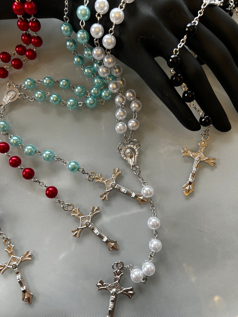May include: Five different rosaries with silver crosses and beads in red, white, black, and blue.