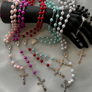 May include: A set of six pearl rosaries with silver chains and crosses. The rosaries are in various colours, including pink, purple, red, blue, white, and black.