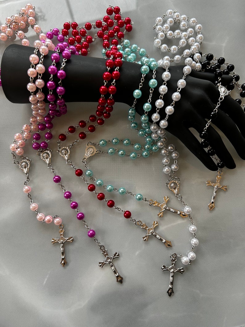May include: A set of six pearl rosaries with silver chains and crosses. The rosaries are in various colours, including pink, purple, red, blue, white, and black.