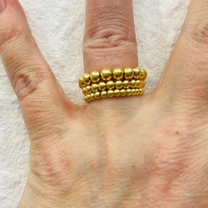Könnte beinhalten: Ein Satz von drei goldenen Perlenringen, die auf einem Finger gestapelt sind.