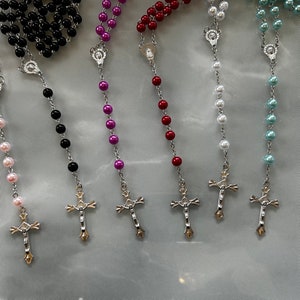 May include: Seven different rosaries with silver crosses and beads in various colours, including pink, black, purple, red, white, and blue.