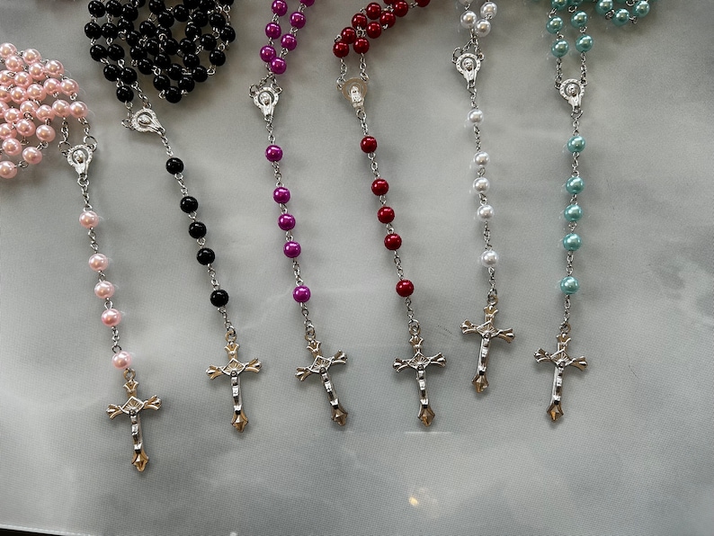 May include: Seven different rosaries with silver crosses and beads in various colours, including pink, black, purple, red, white, and blue.