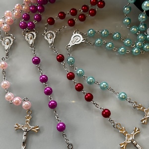 May include: Three silver rosaries with different coloured beads. The rosaries have silver crosses and centrepieces. The beads are pink, purple and blue.