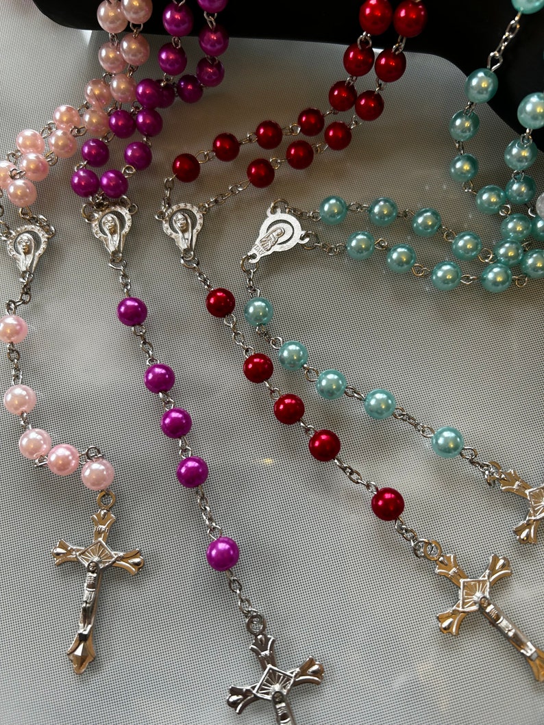 May include: Three silver rosaries with different coloured beads. The rosaries have silver crosses and centrepieces. The beads are pink, purple and blue.