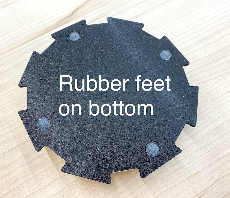 May include: Black, geometric-shaped object with a textured surface. The text "Rubber feet on bottom" is printed in white. Four small, gray rubber feet are visible on the bottom of the object.