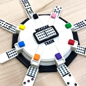May include: A Mexican Train dominoes game set. The white game board has a black border and colorful markers. The dominoes are white with black dots. The words "Mexican Train" are printed on the board.
