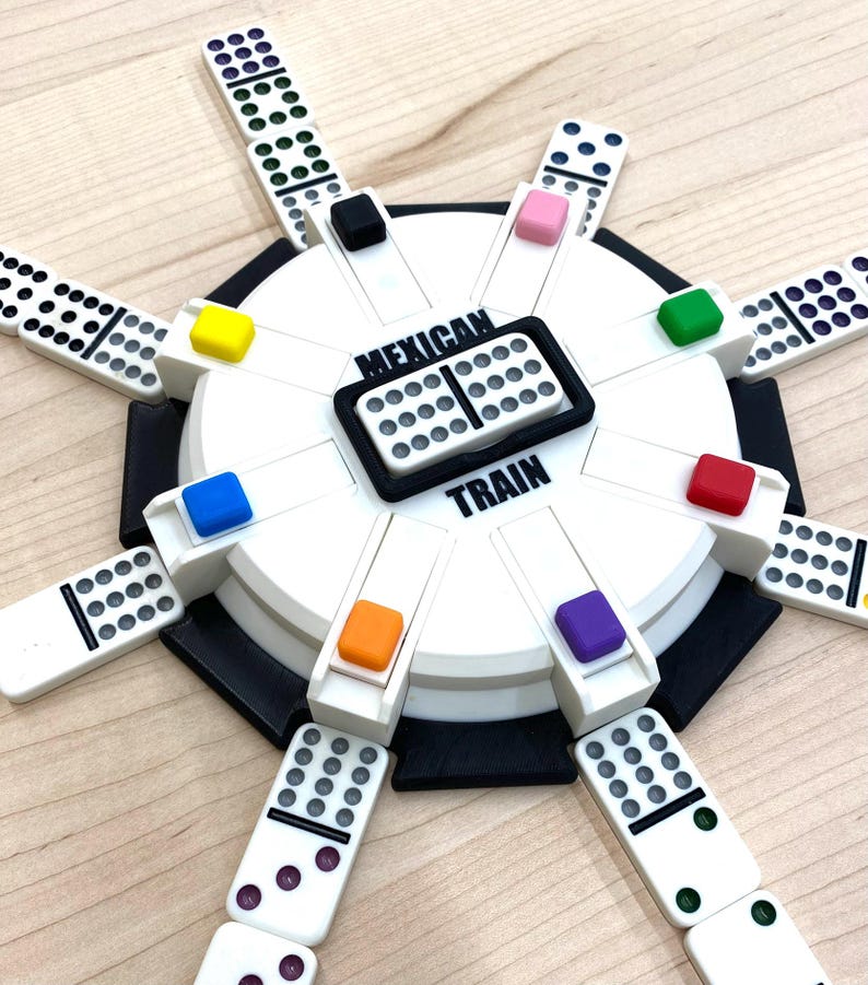 May include: A Mexican Train dominoes game set. The white game board has a black border and colorful markers. The dominoes are white with black dots. The words "Mexican Train" are printed on the board.