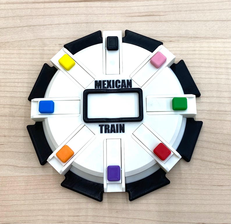 May include: A white and black Mexican Train dominoes game board with the words "MEXICAN TRAIN" printed on it. The board has a rectangular black frame in the center and colored pegs in yellow, blue, pink, green, red, orange, and purple.