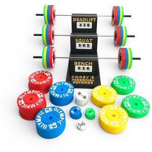 May include: A weightlifting set with barbells and weight plates in red, blue, yellow, and green. The set includes a display showing personal records for deadlift, squat, and bench press. The weight plates are labeled with their weight in pounds.