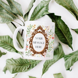 Puede incluir: Taza de cerámica blanca con un diseño floral y un marco dorado adornado con el texto "YOUR MESSAGE HERE".