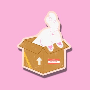 Könnte beinhalten: Ein weißes Kaninchen mit rosa Ohren und Pfoten schaut aus einer braunen Pappbox heraus. Die Box hat ein gelbes Klebeband und einen nach oben zeigenden Pfeil. Ein rotes Etikett auf der Box lautet "PLEASE HANDLE WITH CARE FRAGILE".