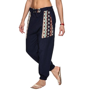 May include: Dark navy blue joggers featuring a drawstring waist and two large side pockets with a cream, brown, and teal geometric patterned fabric. The trousers have a relaxed fit with elasticated cuffs at the ankles, providing a comfortable look.