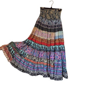 Puede incluir: Una falda larga sin tirantes con un diseño de patchwork vibrante. La falda presenta una variedad de patrones y colores, incluyendo azul, rojo, morado y negro. La falda está colgada en una percha.