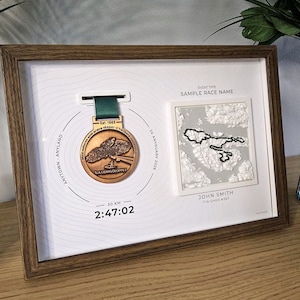 Könnte beinhalten: Ein gerahmtes Display mit einer bronzefarbenen Medaille mit grünem Band und einem quadratischen 3D-Relief einer topografischen Karte. Der weiße Hintergrund enthält den Text Sample Race Name, John Smith, Finisher #367, 30 KM und 2:47:02.