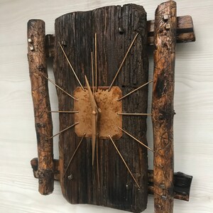Puede incluir: Un reloj de madera r&uacute;stico con una cara de cobre y manecillas doradas. El reloj est&aacute; montado en una pieza de madera recuperada con dos ramas de madera a cada lado.