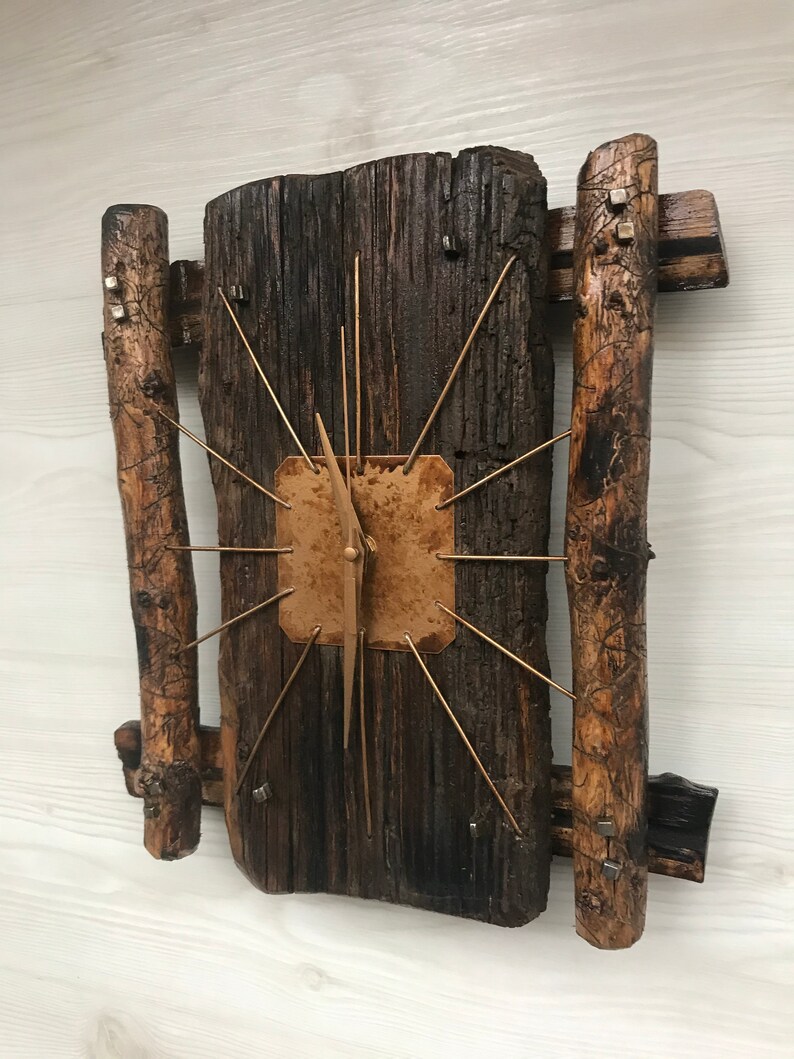 Puede incluir: Un reloj de madera r&uacute;stico con una cara de cobre y manecillas doradas. El reloj est&aacute; montado en una pieza de madera recuperada con dos ramas de madera a cada lado.