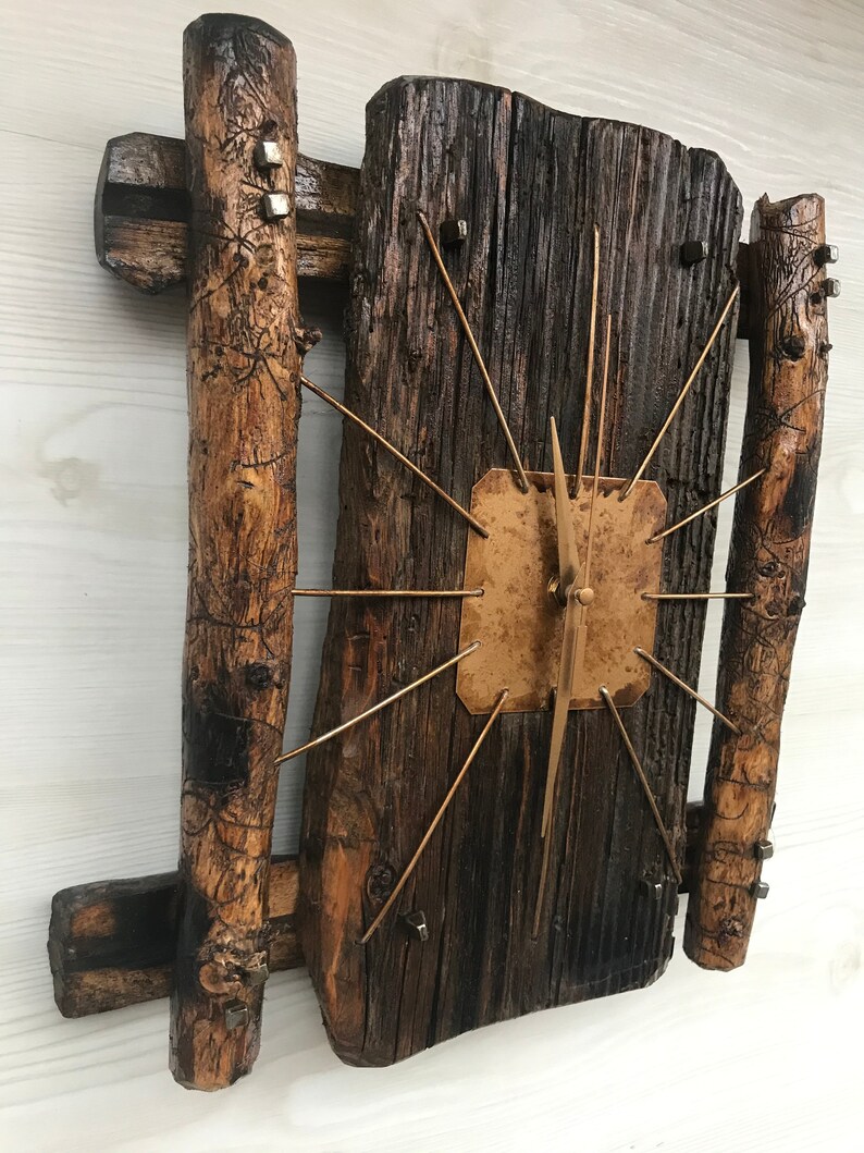 Puede incluir: Un reloj de madera r&uacute;stico con una esfera dorada y agujas de metal. El reloj est&aacute; hecho de madera recuperada y tiene un aspecto &uacute;nico y artesanal.