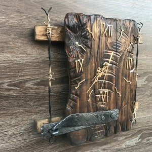 Puede incluir: Un reloj de madera rústico con números romanos y un marco de metal. El reloj está montado en una pared de madera con alambre de púas.