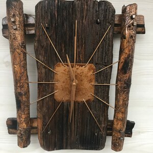 Puede incluir: Un reloj de madera r&uacute;stico con una cara de cobre y manecillas doradas. El reloj est&aacute; montado en un trozo de madera a la deriva con dos trozos m&aacute;s peque&ntilde;os de madera a la deriva a cada lado.