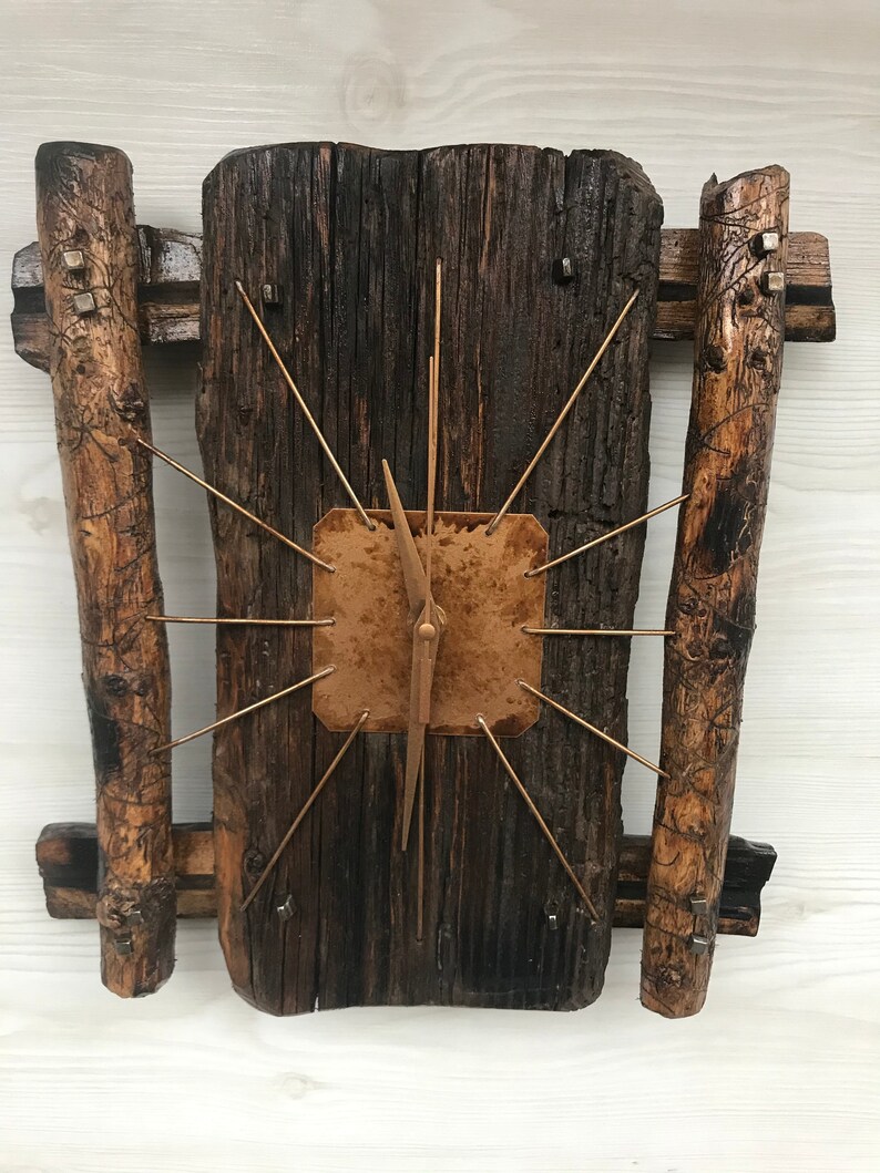 Puede incluir: Un reloj de madera r&uacute;stico con una cara de cobre y manecillas doradas. El reloj est&aacute; montado en un trozo de madera a la deriva con dos trozos m&aacute;s peque&ntilde;os de madera a la deriva a cada lado.
