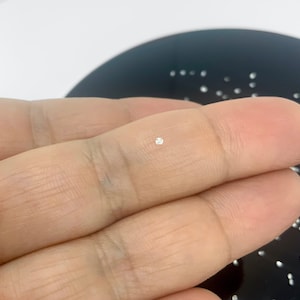 May include: A small, clear, round diamond held between two fingers.
