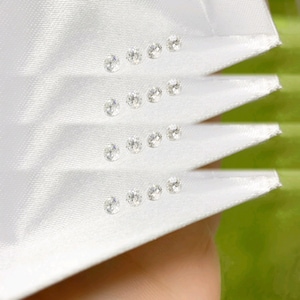 May include: Close-up of white satin fabric with rows of small, sparkling gemstones. The gemstones are evenly spaced and appear to be round-cut. The fabric is folded in a fan-like pattern, creating a textured surface. The background is a soft green.