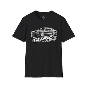 Op de afbeelding: Een zwart t-shirt met korte mouwen en een witte grafische illustratie van een sedan. Onder de auto staat de tekst CEDRIC Y-SERIES in een vet, gestileerd lettertype. Het ontwerp is gecentreerd op de borst van het kledingstuk met een ronde hals.