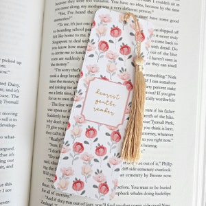 May include: A bookmark with a floral design featuring pink and white flowers on a white background. The bookmark has a gold tassel and a gold inscription that reads "Dearest gentle reader".