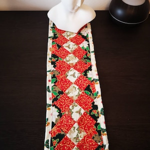 Könnte beinhalten: Ein roter, grüner und weißer Weihnachtstischläufer mit einem Rautenmuster. Der Läufer ist aus Stoff mit einem Blumendesign.