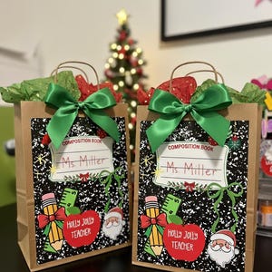 Può includere: Due sacchetti regalo di carta marrone con fiocchi verdi e carta velina rossa e verde. Ogni sacchetto presenta un design a quaderno con il nome "Ms. Miller" e grafiche a tema natalizio, tra cui una matita, una mela e Babbo Natale.