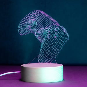 May include: A 3D printed, wireframe style, gamer controller night light with a white base. The light is illuminated in a blue and purple colour scheme.