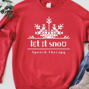 Peut inclure: Sweat-shirt rouge avec un flocon de neige blanc et le texte "Let It Snow Speech Therapy".