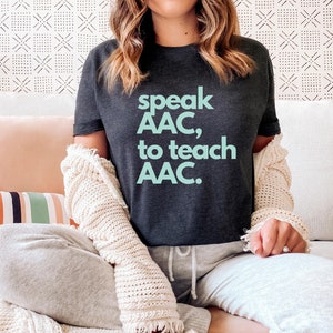 Pu&ograve; includere: Una maglietta grigia scura con il testo "speak AAC, to teach AAC." in azzurro.