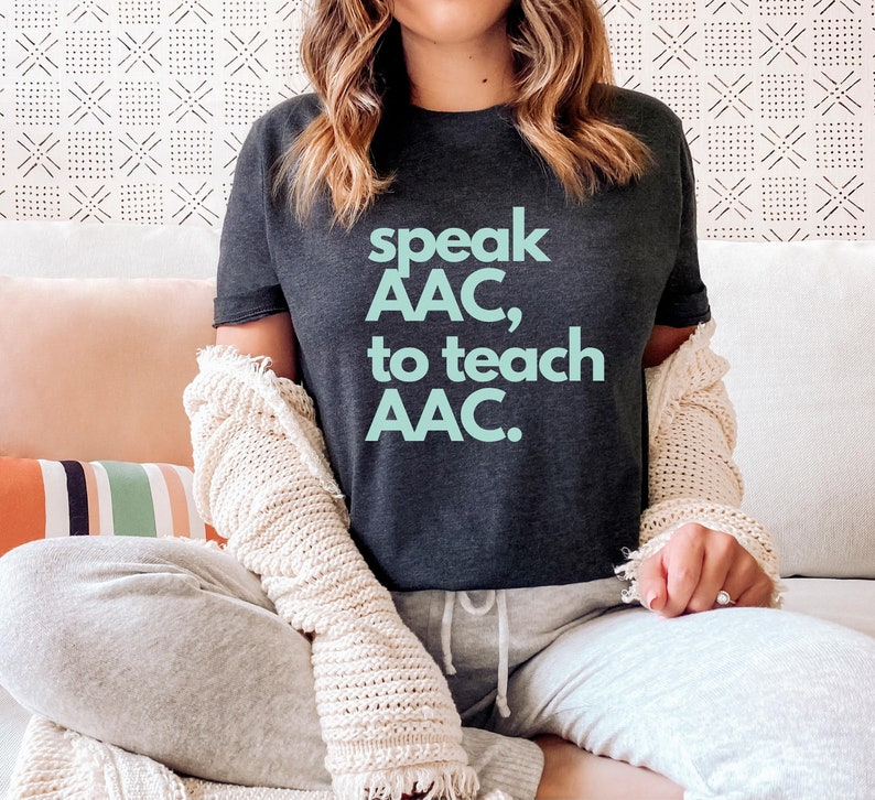 Pu&ograve; includere: Una maglietta grigia scura con il testo "speak AAC, to teach AAC." in azzurro.