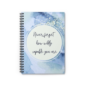 May include: Spiral-bound notebook with a watercolor design in shades of blue and silver glitter accents. The cover features the text "Never forget how wildly capable you are" in a handwritten font. The notebook is designed for writing and note-taking.