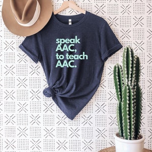 Pu&ograve; includere: Una maglietta blu navy con la scritta "speak AAC, to teach AAC." stampata in azzurro.