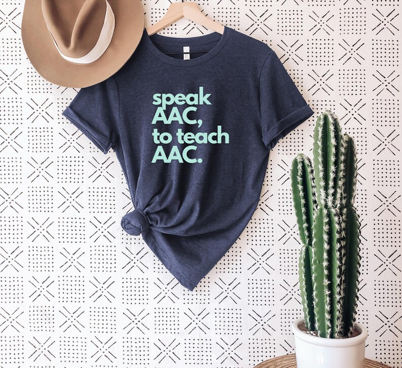 Pu&ograve; includere: Una maglietta blu navy con la scritta "speak AAC, to teach AAC." stampata in azzurro.