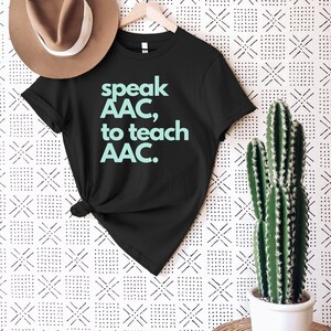 Pu&ograve; includere: Maglietta nera con il testo "speak AAC, to teach AAC." in azzurro.