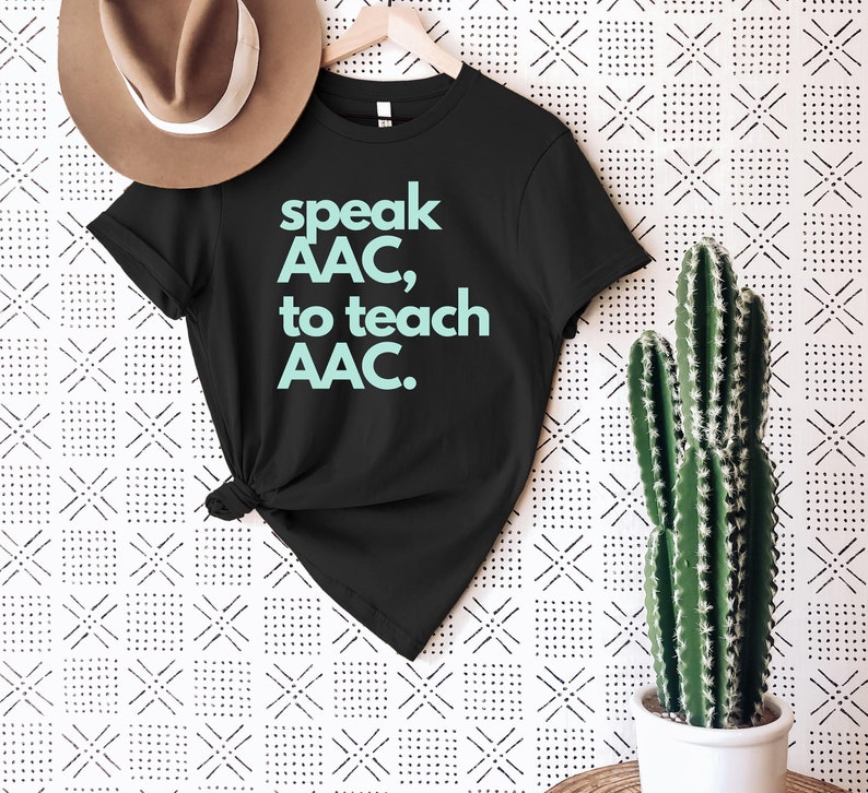 Pu&ograve; includere: Maglietta nera con il testo "speak AAC, to teach AAC." in azzurro.