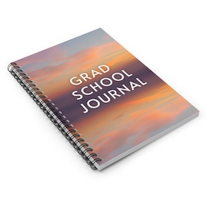 May include: A spiral bound journal with a colourful sunset sky background. The text "GRAD SCHOOL JOURNAL" is printed in white on the cover.