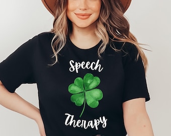 May include: Black t-shirt featuring a watercolor-style green shamrock and the words "Speech Therapy" in white script. The design is centered on the front of the shirt. The shirt is made of a soft material.
