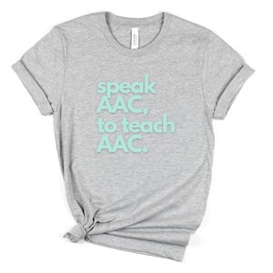 Pu&ograve; includere: Maglietta grigia con il testo "speak AAC, to teach AAC." in azzurro.