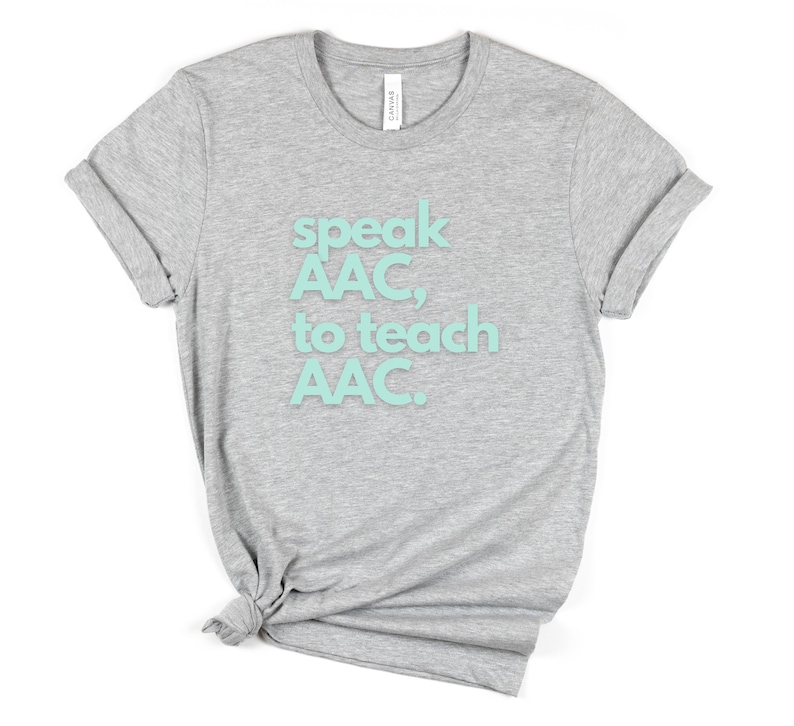Pu&ograve; includere: Maglietta grigia con il testo "speak AAC, to teach AAC." in azzurro.